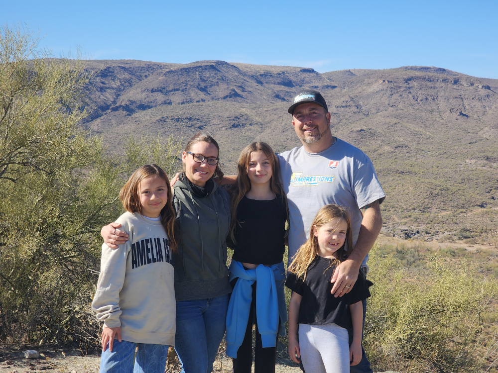 A mother, father, and their three daughters pose in front of rugged desert terrain