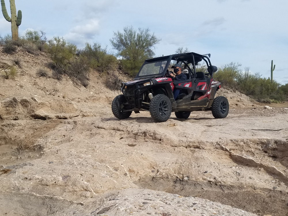 A red side-by-side UTV rides across the rugged desert terrain